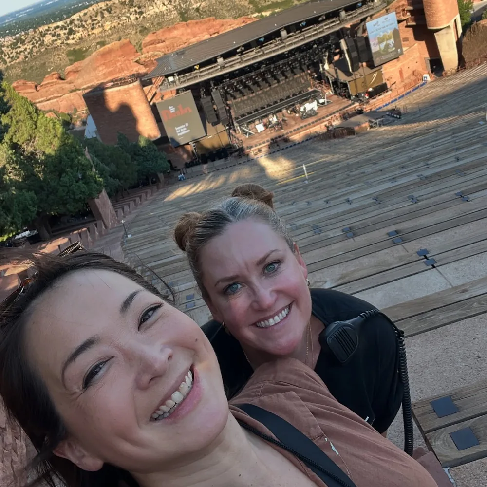 Selena Moshell and a crew member with a radio smiling high above an outdoor red rock amphitheater and its stage before the show