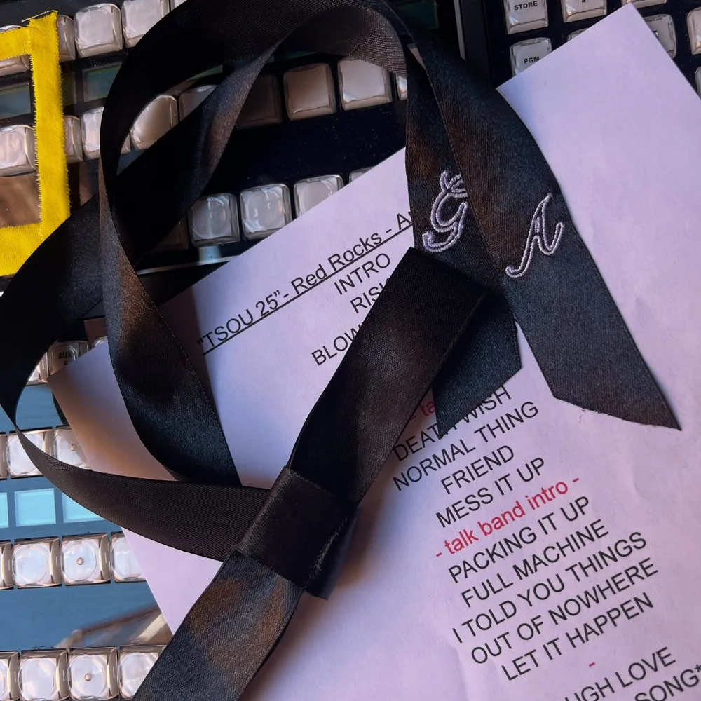 A tour setlist and a black ribbon embroidered GA resting on a lit video switcher